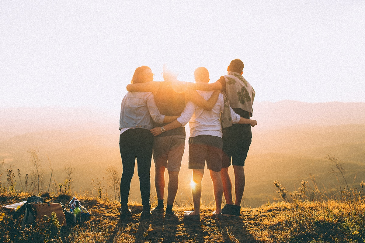 4 young adults hugging at sunset