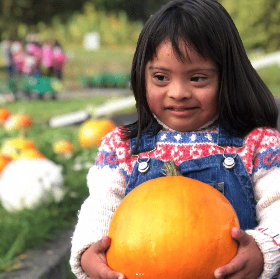 Little girl smiling while holding her pumpkin at the pumkin patch.