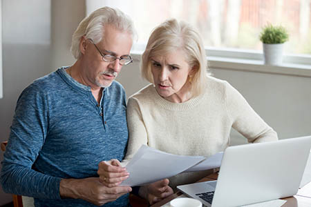 Serious elder husband and wife read bank documents at home