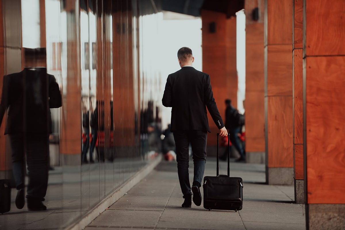Going to airport terminal. Confident businessman traveler walking on city streets and pulling his suitcase drinking coffee and speaking on smartphone